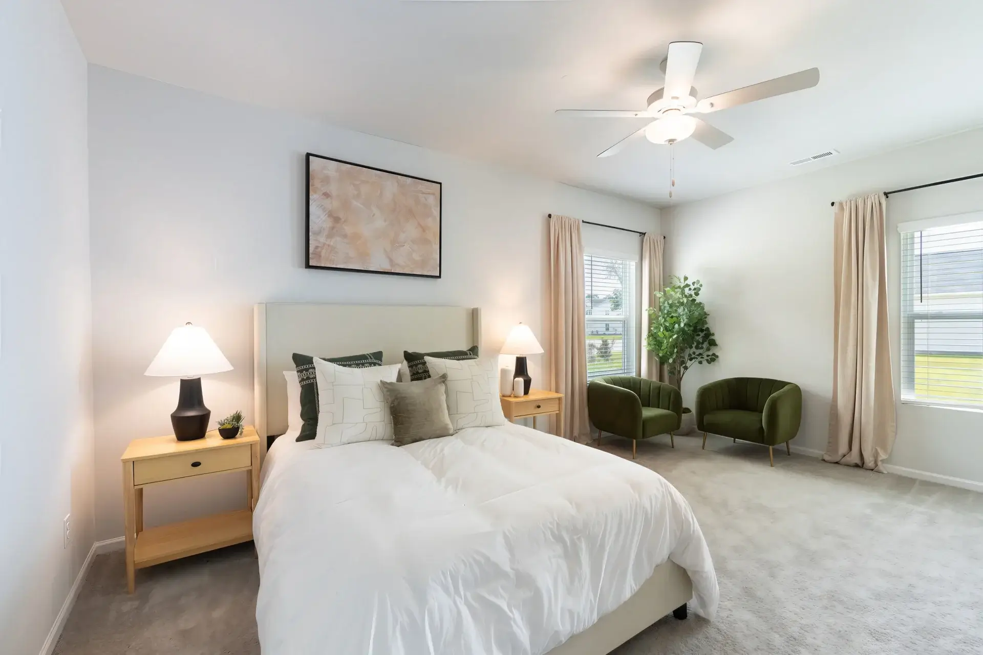 Pet-Friendly Single-Family Homes for Rent in Bolivia, NC - Carolina Crossing - Bedroom with Upholstered Headboard, Nightstands, Table Lamps, Ceiling Fan, Armchairs, Plant, and Carpet Flooring.